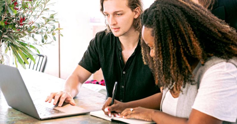 Collaborative Learning - Man Working on Laptop while Woman Takes Notes