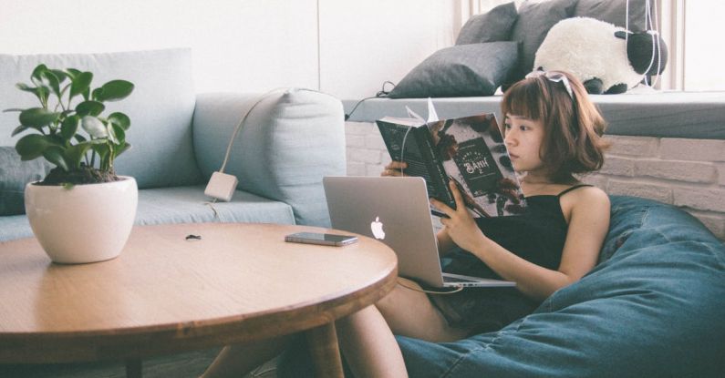 Mobile Learning - Woman Sitting on Bean Bag White Using Macbook in Front of Round Table With Green Leafed Plant