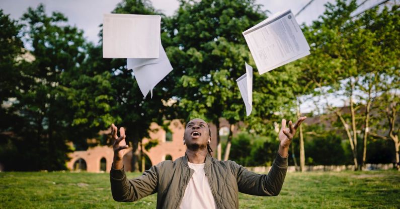 Academic Goals - Happy young black male freelancer throwing papers while celebrating successful project during remote work in green park