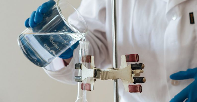 Practice Tests - Crop African American laboratory technician in protective goggles pouring transparent fluid into flask while standing in front of colorful test tubes with reagents