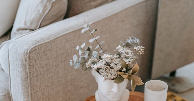 Textbook Editions - Cozy sofa with decorative cushions near stump with books and blooming flowers in vase in house room