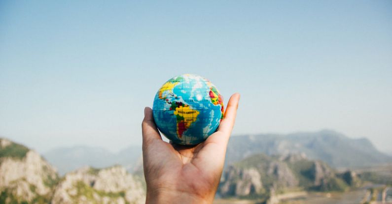 International Editions - Person Holding World Globe Facing Mountain